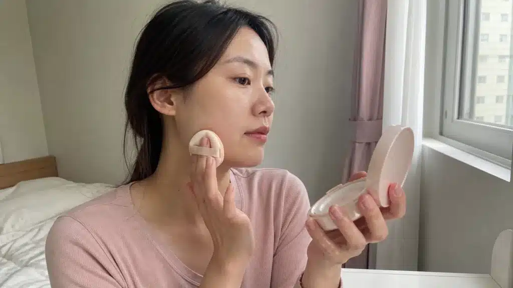 자연광에서 쿠션 퍼프로 턱선의 피부 표현을 확인하는 여성